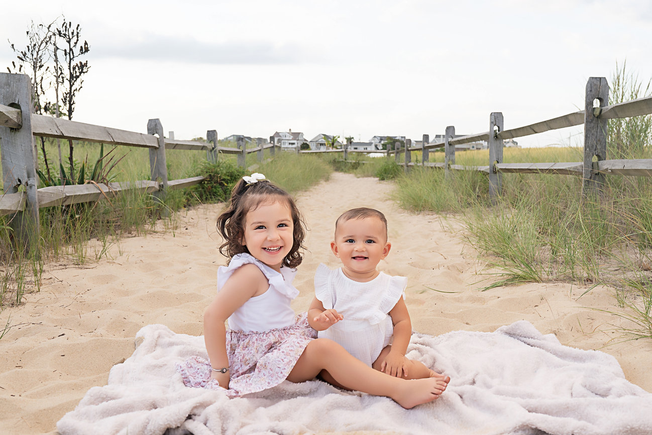 Older sibling holding baby sibling on a soft, sandy beach