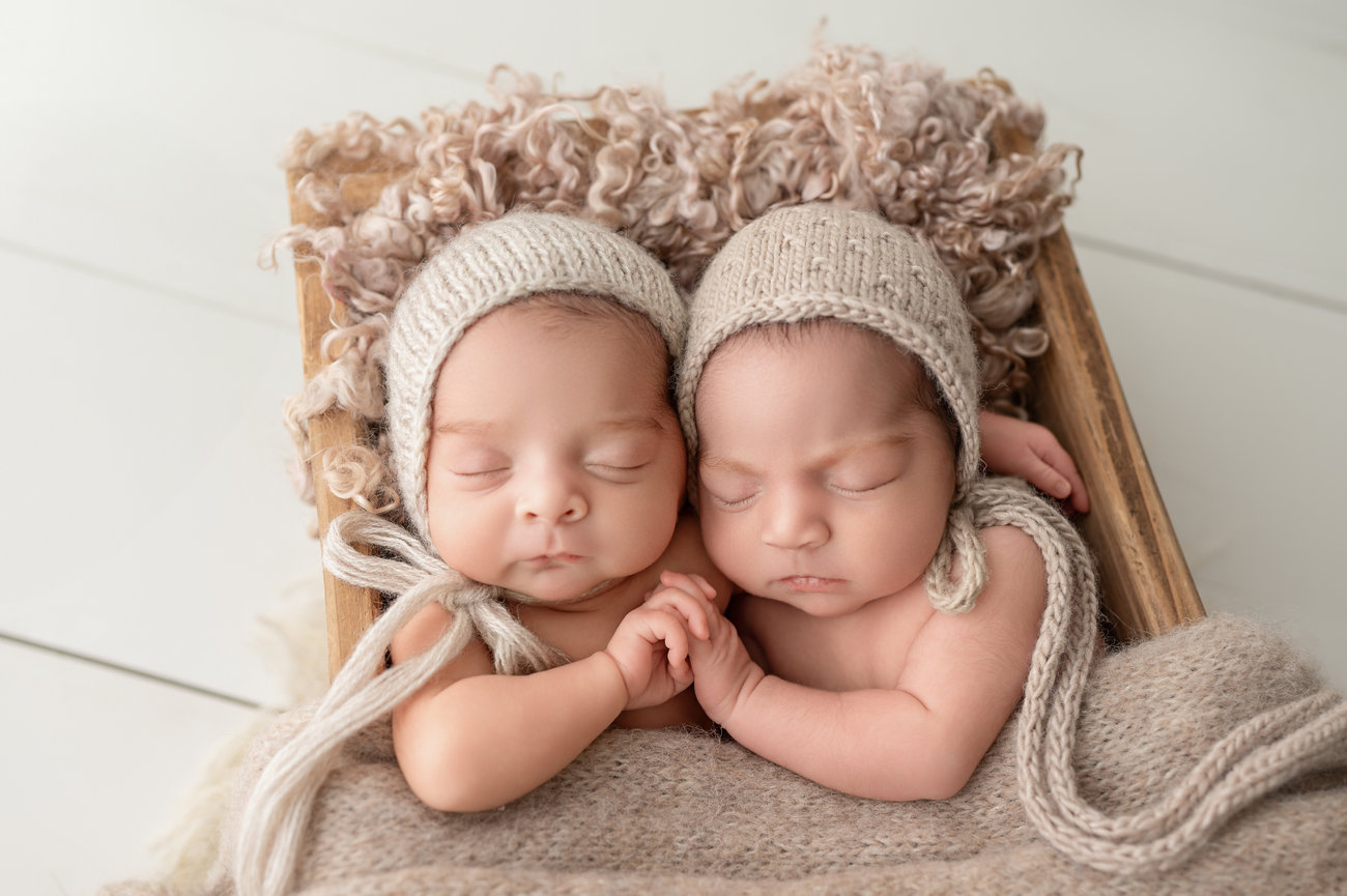 Fine art newborn photo of twin babies wrapped in cable-knit wrap and posed in antique box with soft layering