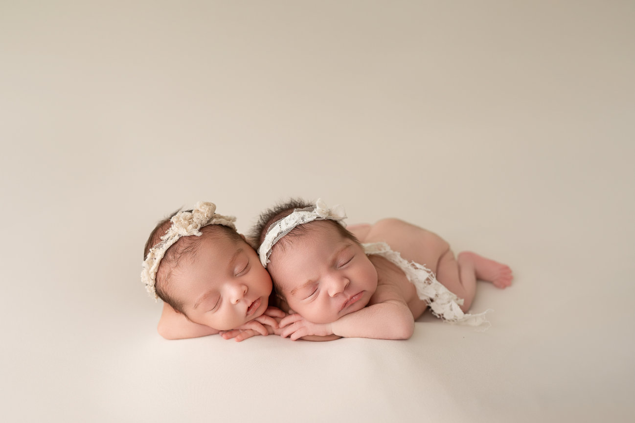 Twin newborns posed with hands under their chins on a soft neutral backdrop during studio session in Monmouth County, NJ, capturing symmetry and connection