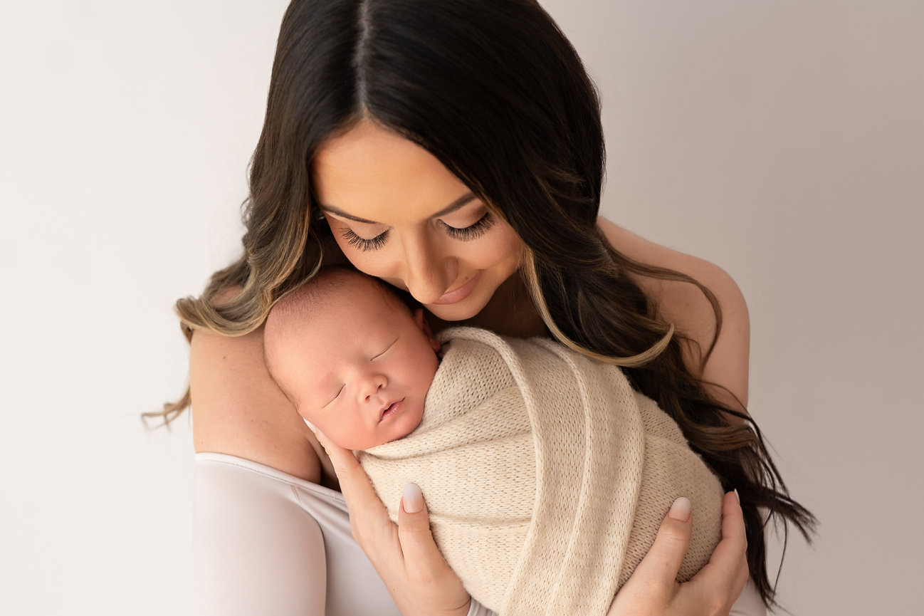 Mother holding newborn baby close with eyes closed, capturing the quiet strength of early motherhood