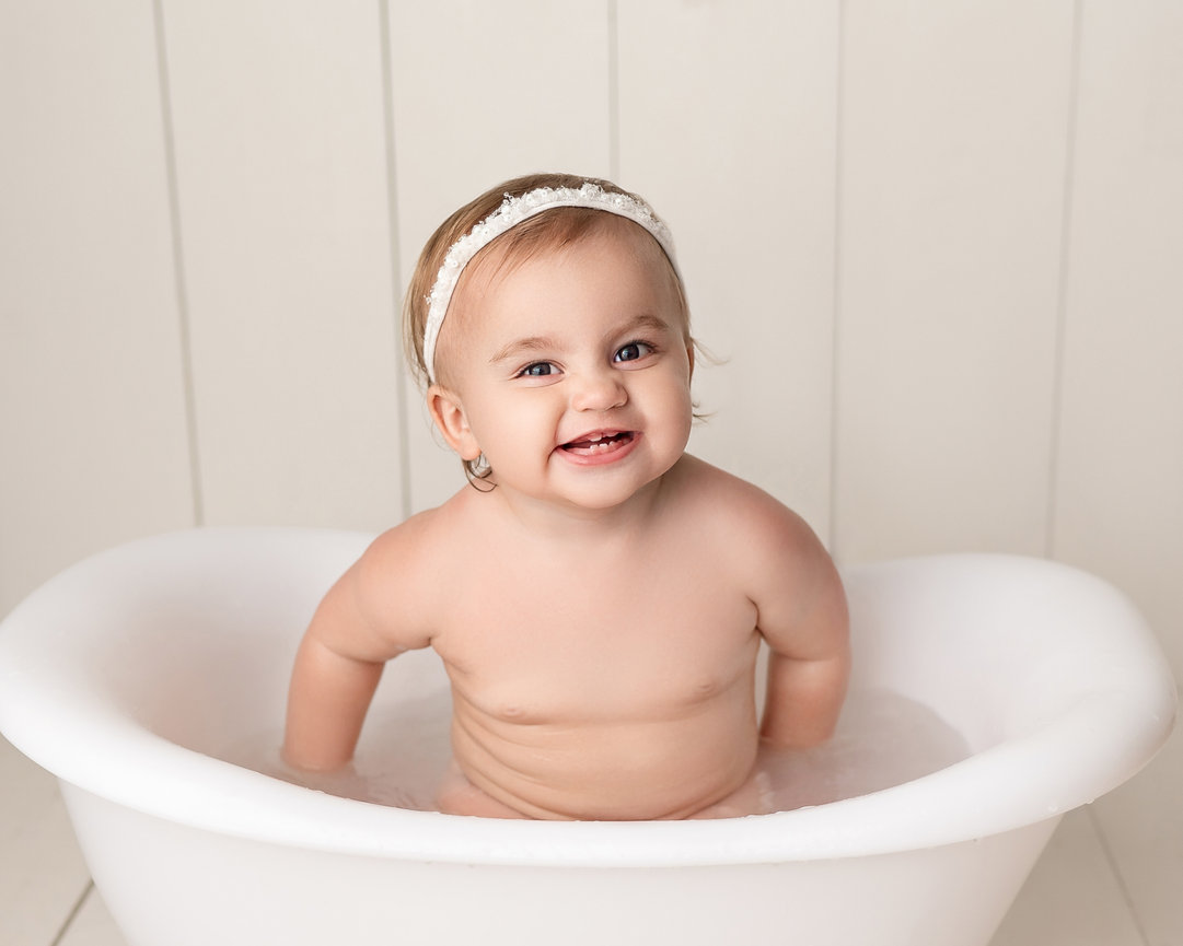 Baby laughing while rinsing off frosting in white bathtub in Summit, NJ photography studio