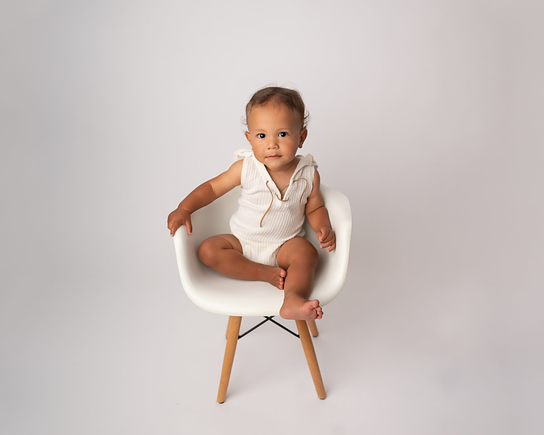 One-year milestone portrait before cake smash on modern white chair in Manasquan studio