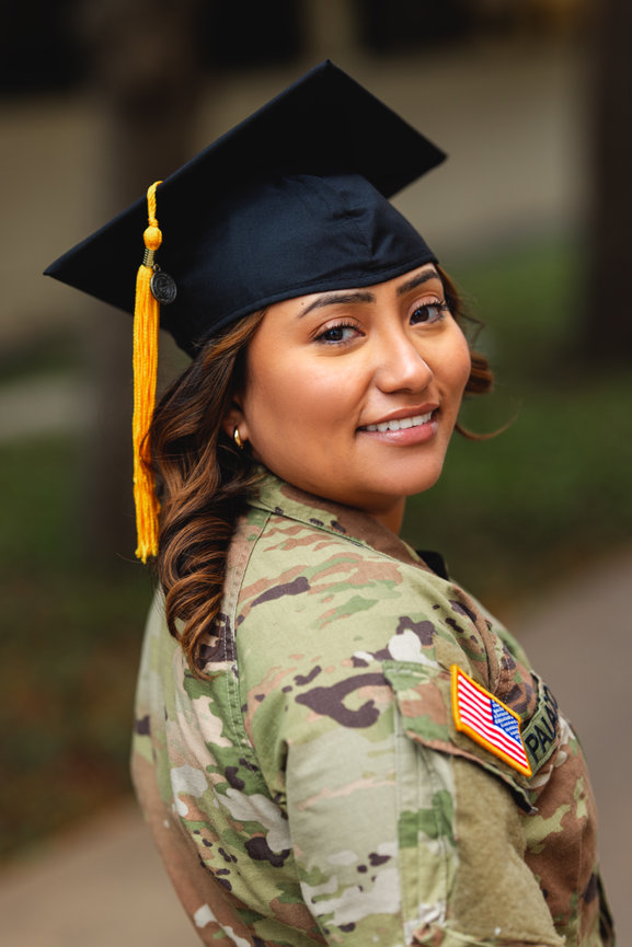 Servicewoman in military uniform smiles, wearing a graduation cap, celebrating academic achievement outdoors at the University of Texas at Dallas