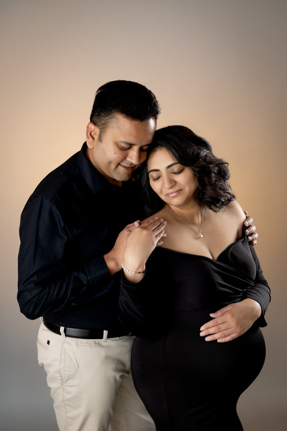 A couple embraces, with the woman holding her pregnant belly, against a soft gradient background.