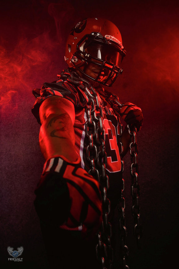 High school football player in helmet and uniform with chains and red smoke for senior sports photos in Green Bay, Wisconsin.