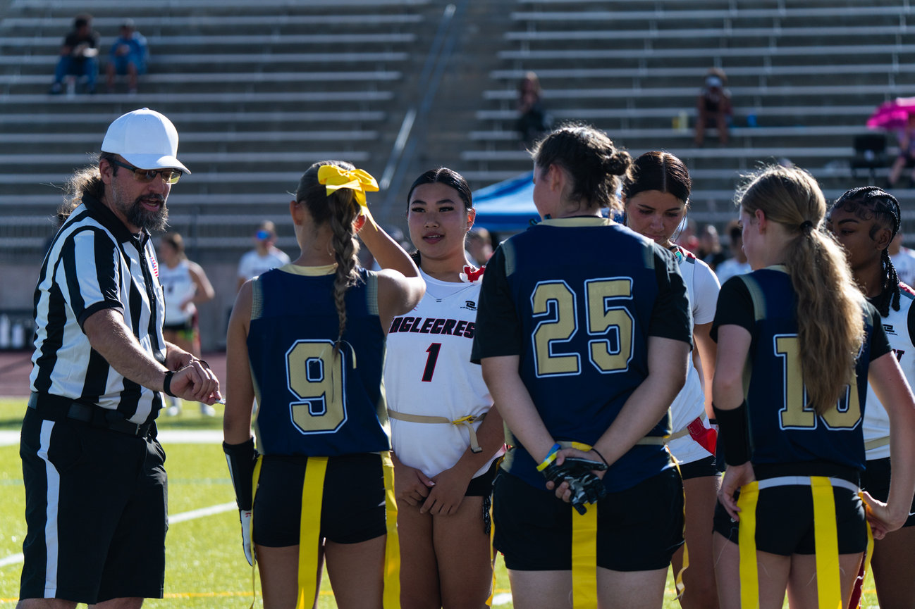 Flag football players and a referee gathered at midfield before a play.