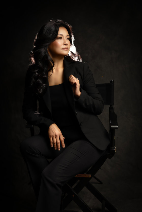 Woman in a black suit seated on a chair against a dark background, looking confidently to the side. fort worth branding headshot