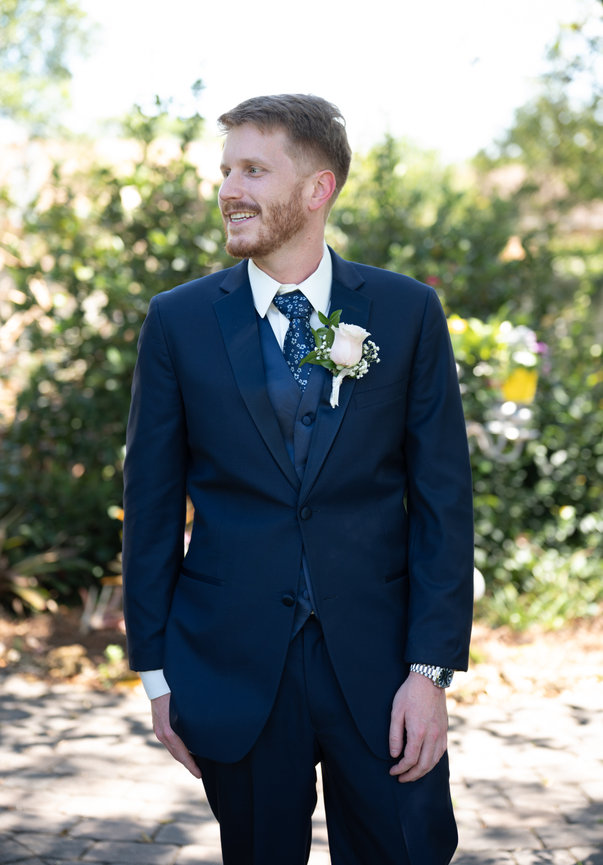 Groom in a navy suit standing outdoors at a wedding venue.