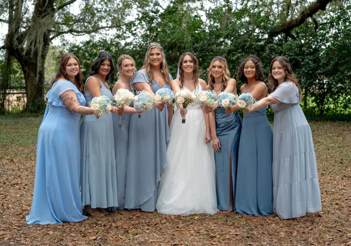 Bride standing with her bridesmaids in matching blue dresses outdoors.
