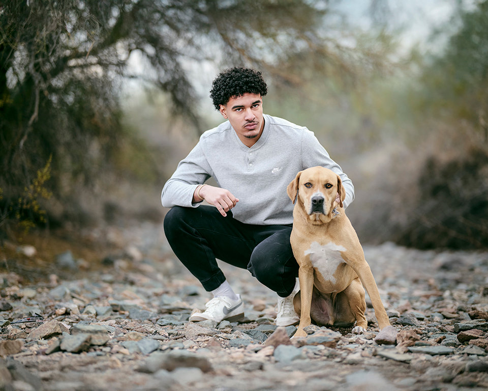 High school senior boy kneeling in desert with golden retriever