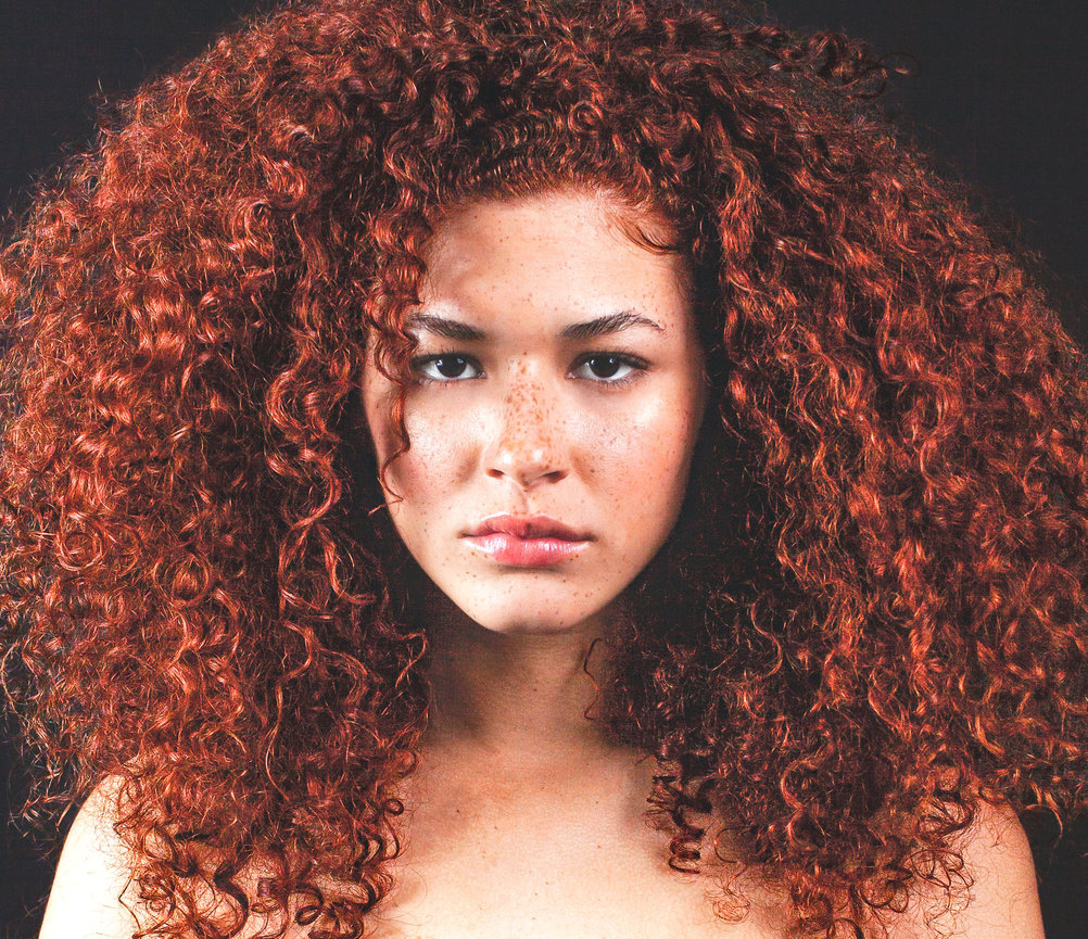 Mixed Model with curly bright red hair in portrait looking intently at camera in photo shot by Sara Racey Photography