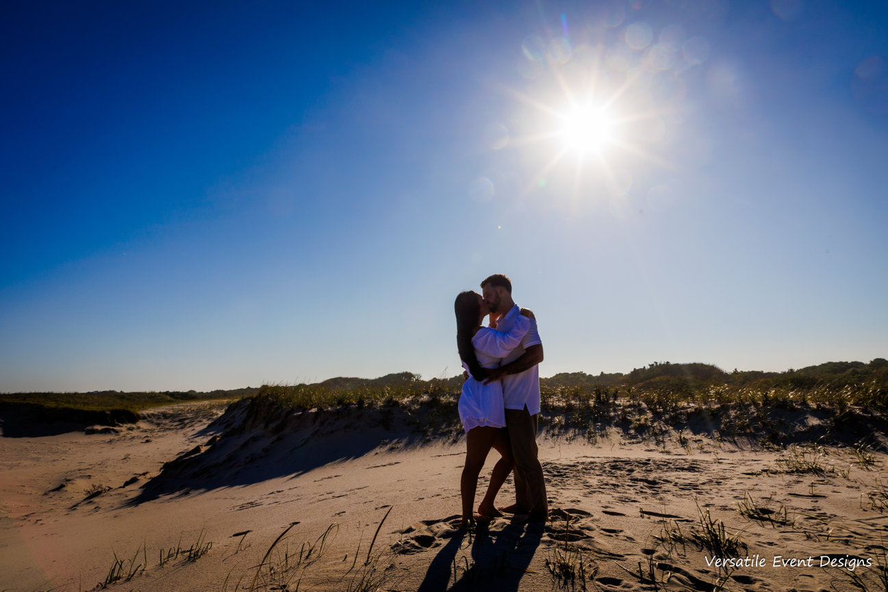 Bride and groom silhouetted on a sand dune under bright sun