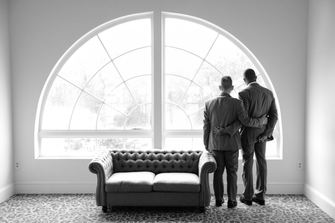 Groom and groomsman beside a tall arched window at a New Jersey wedding venue