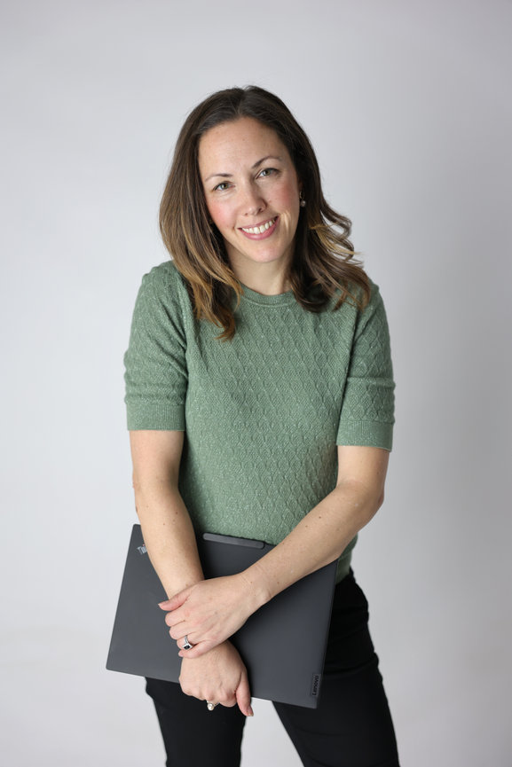 Smiling woman in a green sweater holding a laptop against a plain background. headhshot photoshoot melbourne