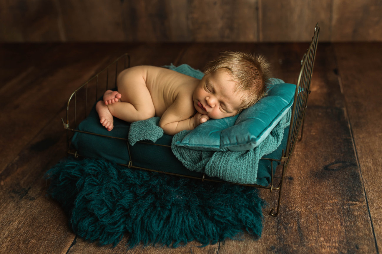 Newborn baby laying against fuzzy green blankets