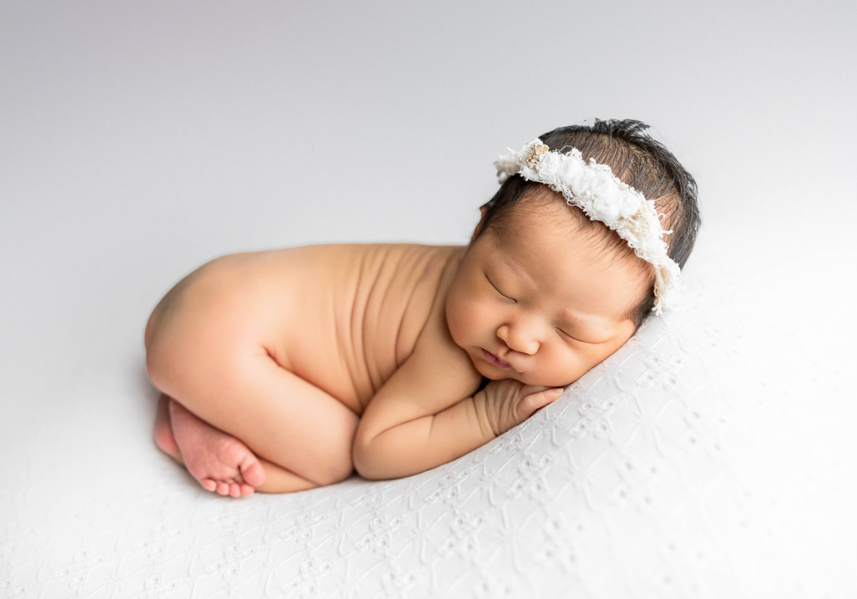 Newborn baby laying on stomach and resting against white backdrop