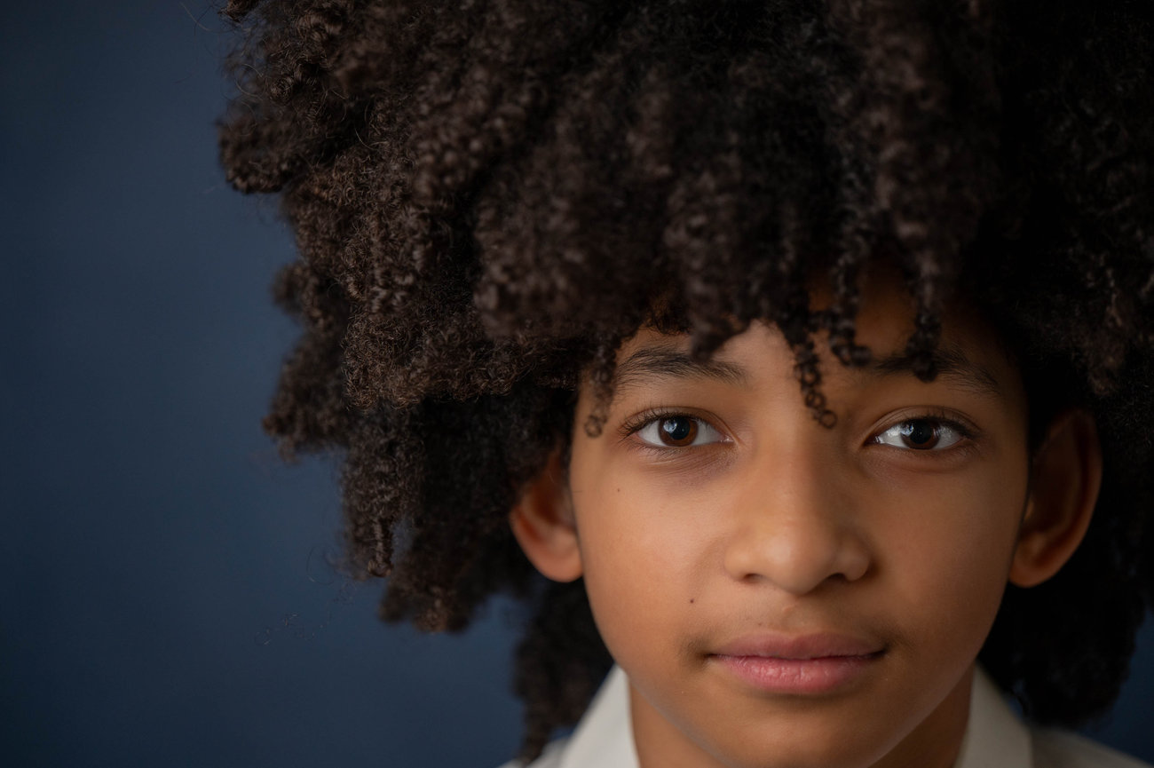 Young person with curly hair against a dark blue background in the style of jo hayes images charlotte portrait modeling fashion event photography