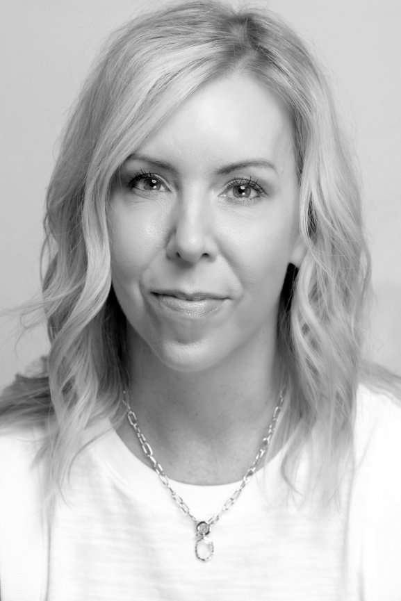 Black and white headshot of a blonde woman wearing a chain necklace on a plain background