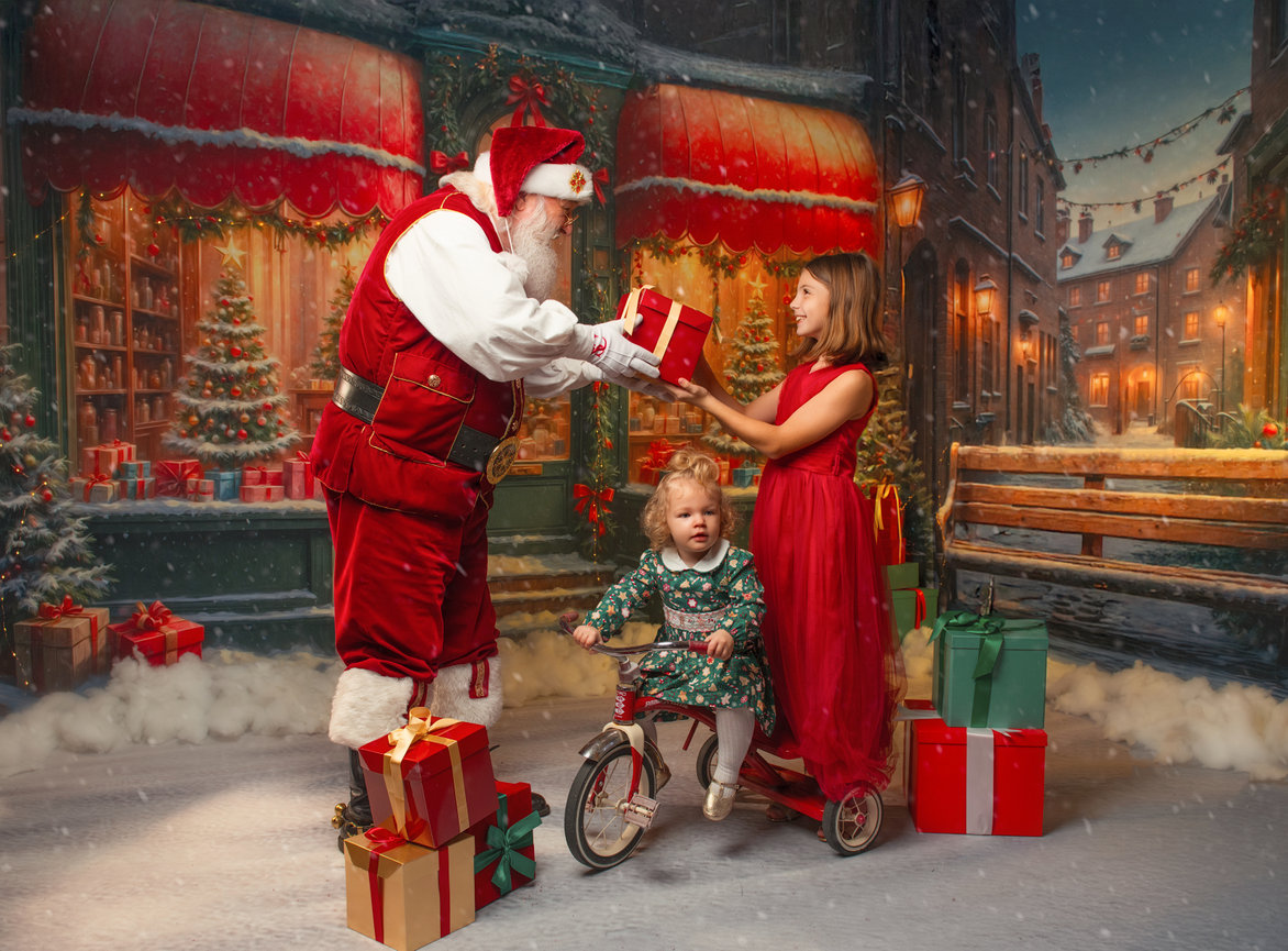 Santa giving a gift to a girl and child in a snowy Christmas street with festive shopfronts during a Baltimore christmas photography session.