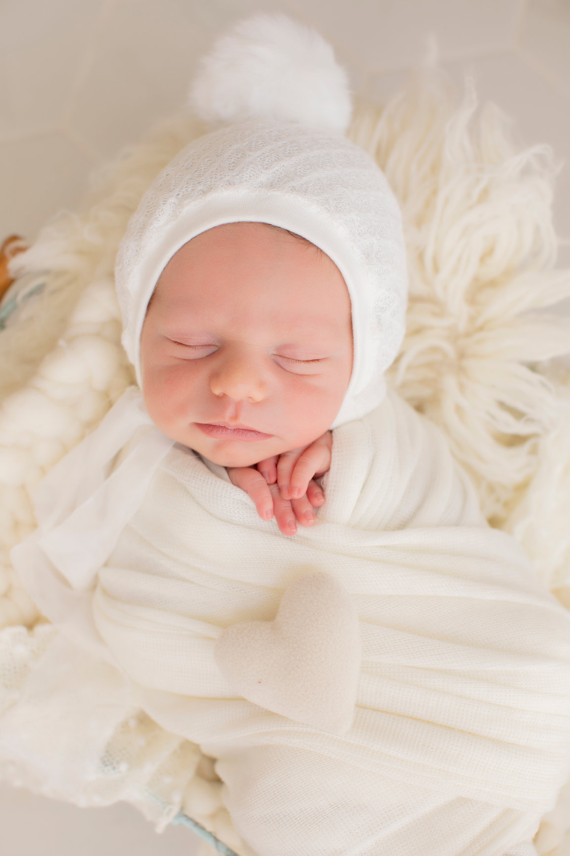 Close-up of a sleeping newborn in an ivory bonnet and wrap.