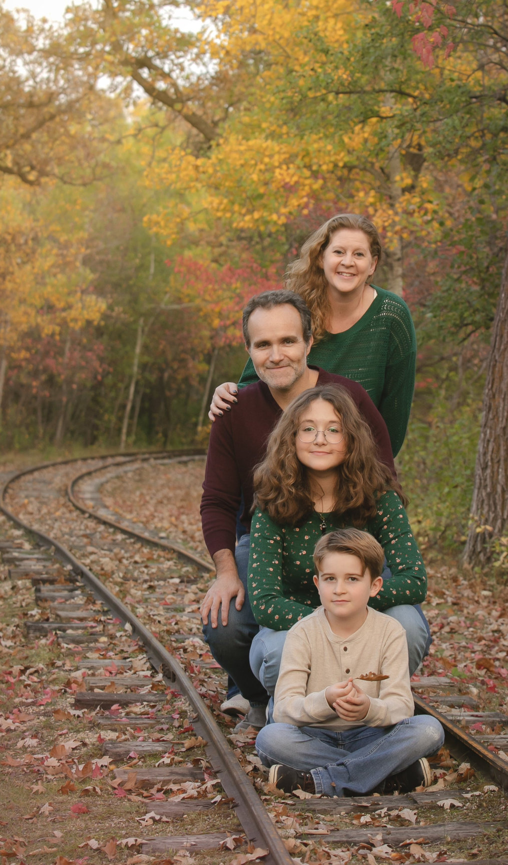 A family of four together outdoors among colourful autumn trees.