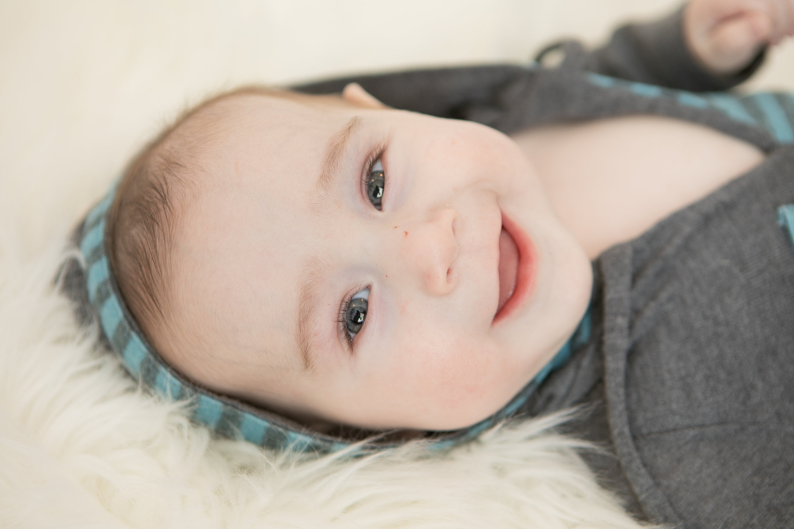 Baby in a dark outfit smiling on soft cream fur