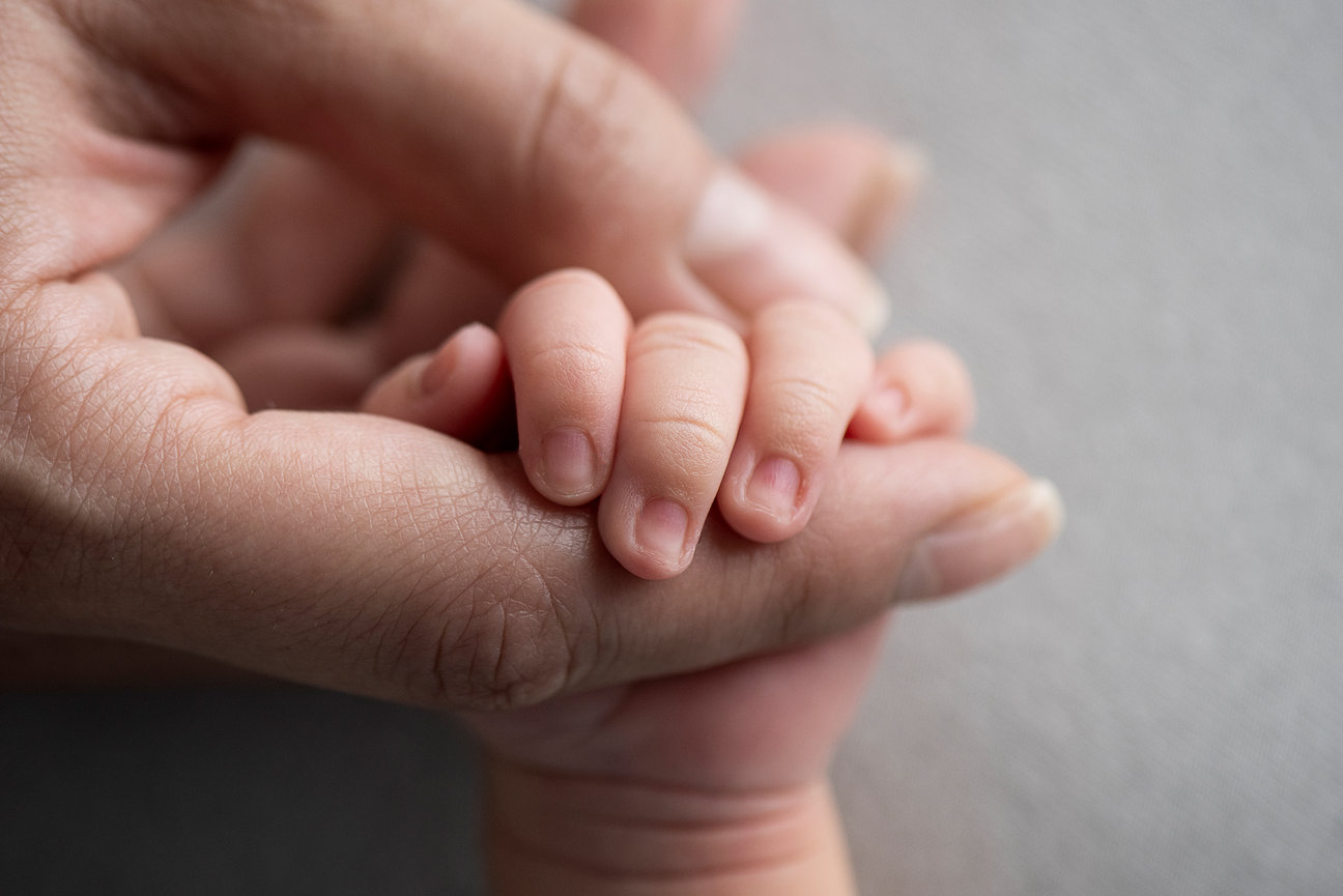A close-up image captures a small babys hand gently gripping an adults finger, showcasing the contrast in size and the tender connection between them. The softly blurred background evokes the serene charm of Deer Park, Illinois.