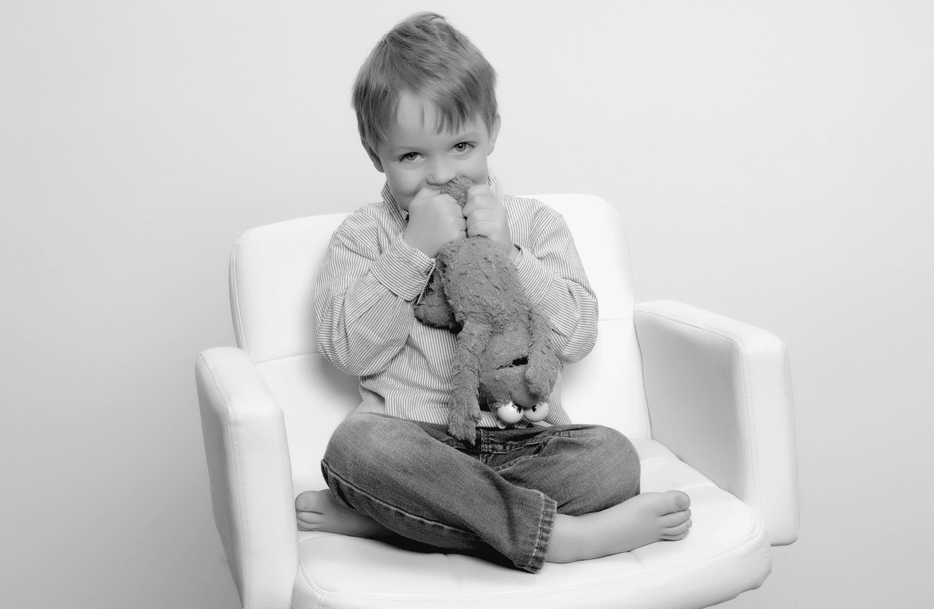 A young boy in jeans biting his Elmo stuffed animal.
