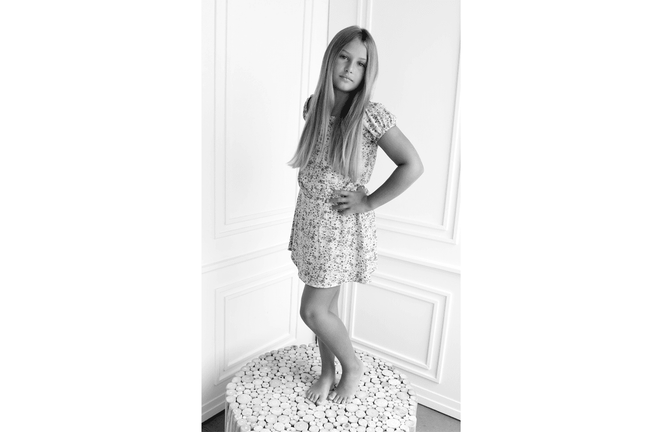 A pre-teen girl in a floral summer dress stands self-assured during her children's photo session at Kliks.