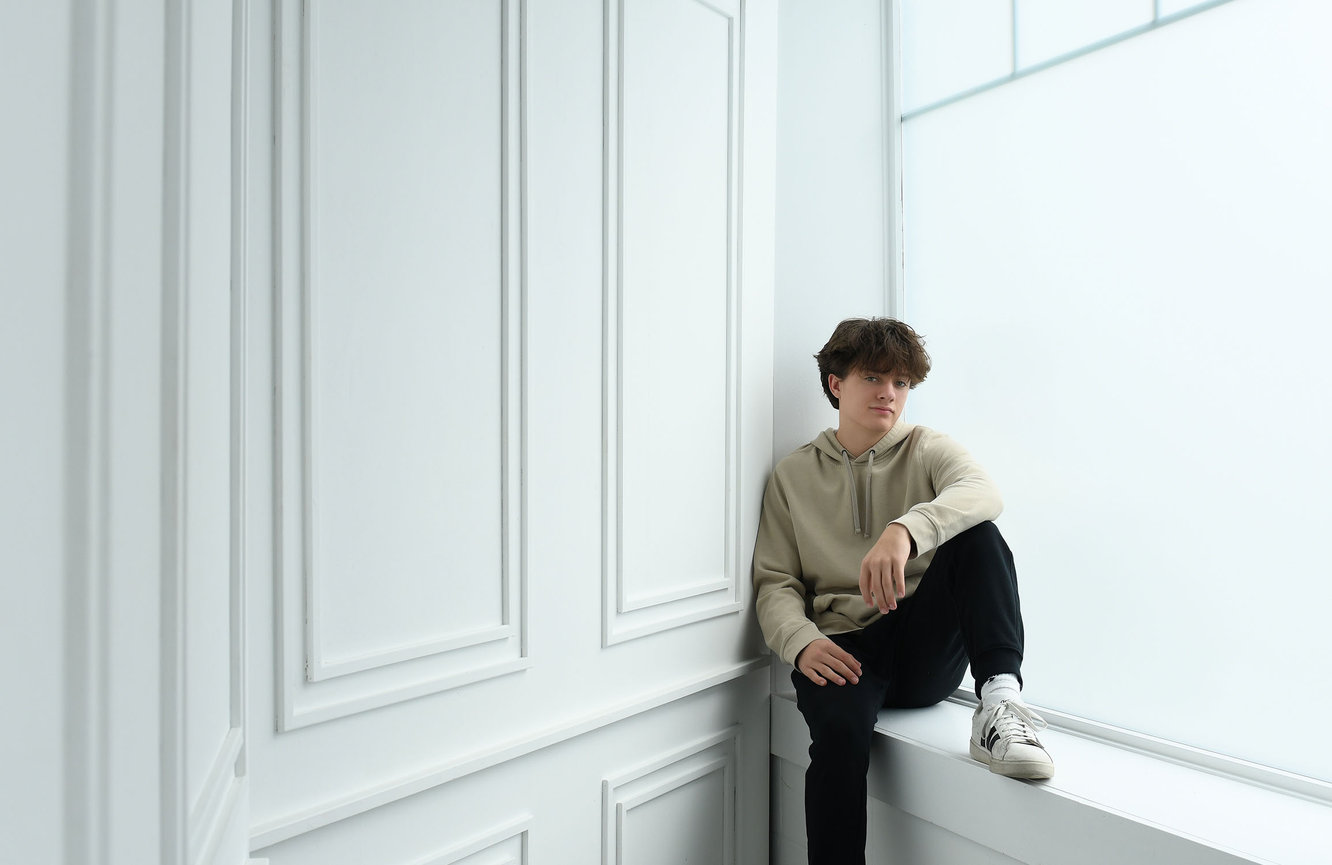 A boy with tousled hair sits in the window sill for his high school senior photos at Kliks Photography in Cedar Rapids, Iowa.