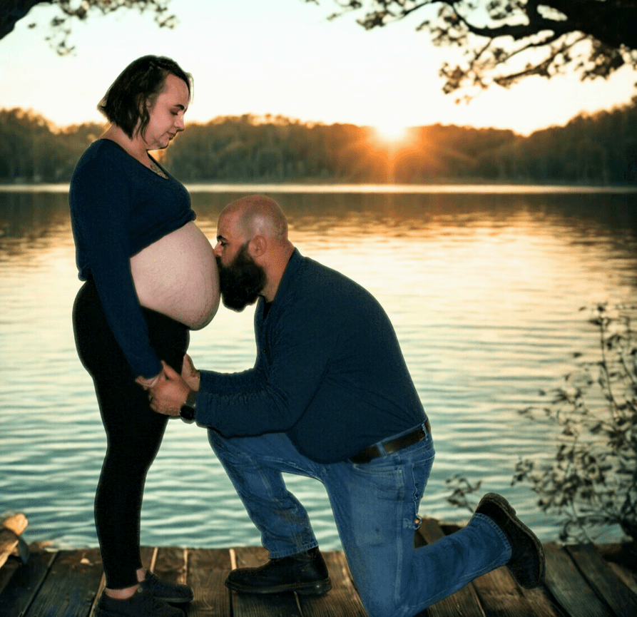 Pregnant couple by a lake during sunset