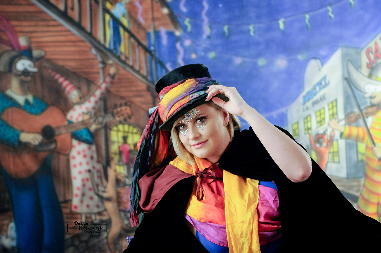 Gypsy lady posing in front of a Mardi Gras style backdrop for an environmental portrait.