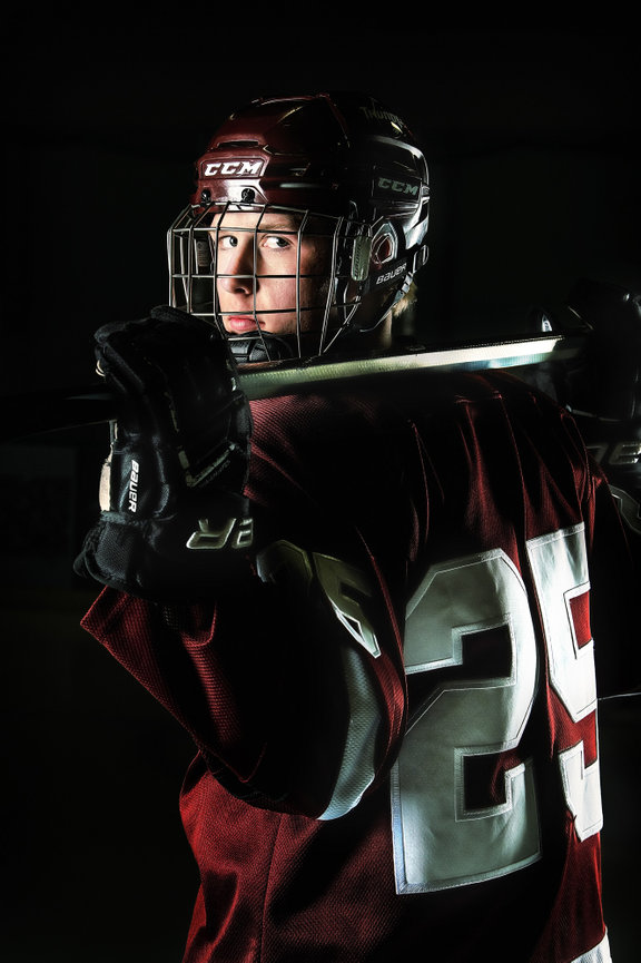 Lakeview Technology Academy senior in maroon jersey and helmet, holding a stick over shoulders, looks back for his senior pictures.
