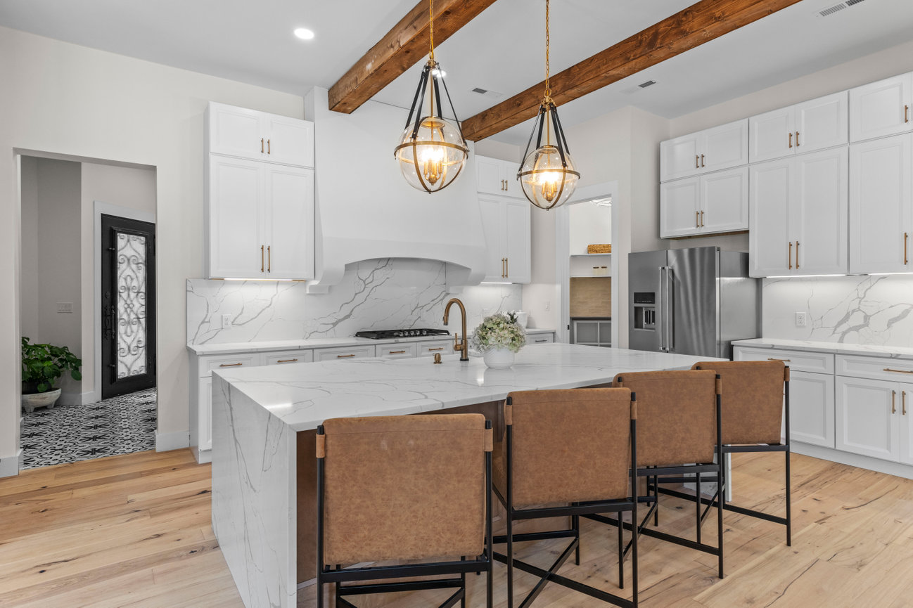 Modern kitchen with white cabinets, marble island, pendant lights, and wood beam ceiling
