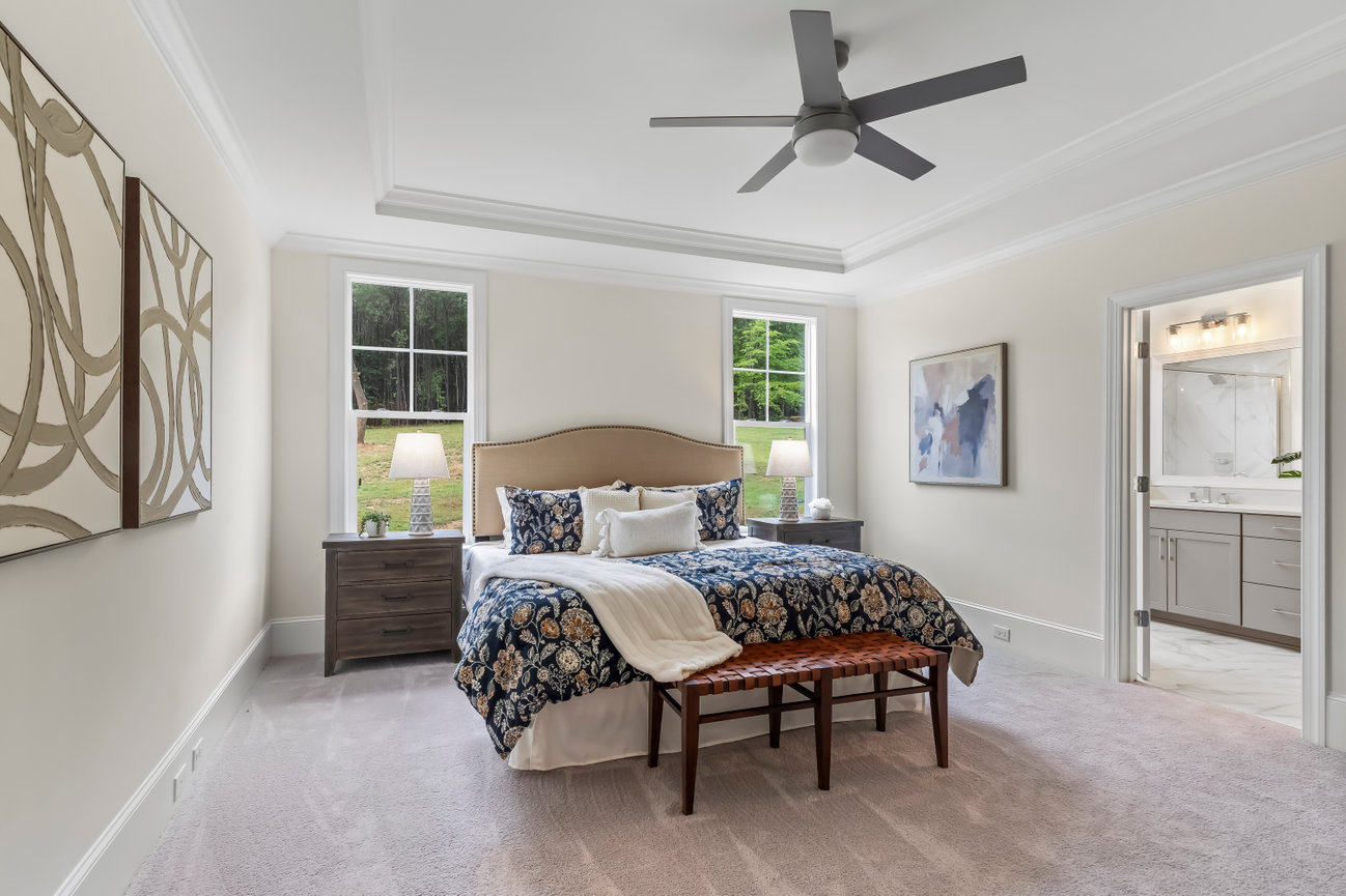 Bright modern bedroom with king bed, ceiling fan, windows, and an attached bathroom view