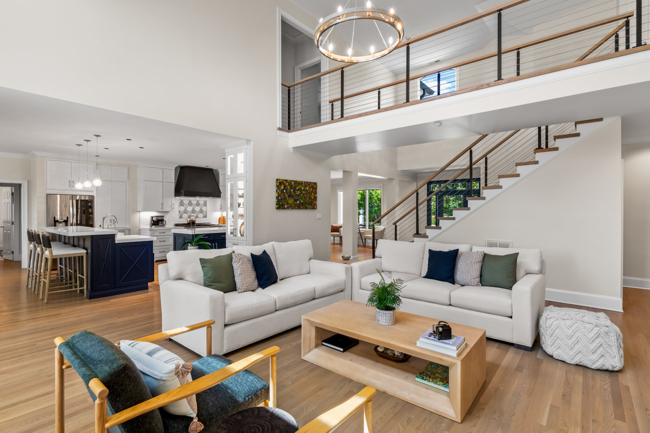 Bright open-concept living room with staircase, modern kitchen, white sofas, and wood floors