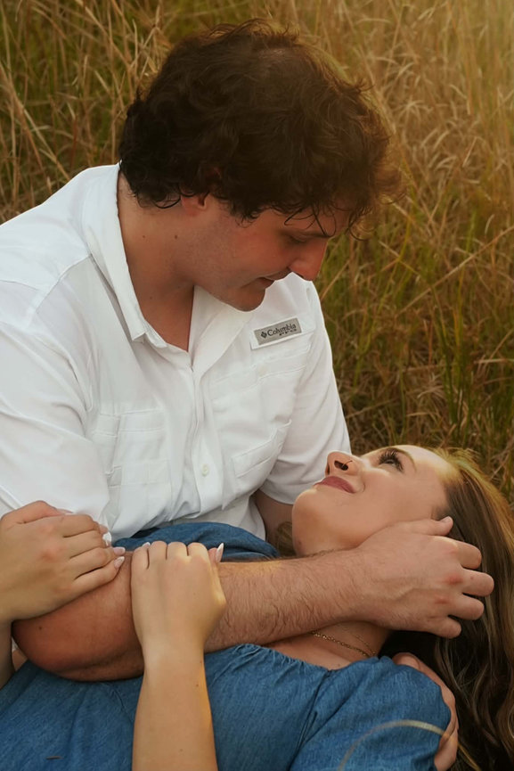 Groom leaning over the bride as they relax in tall grass.