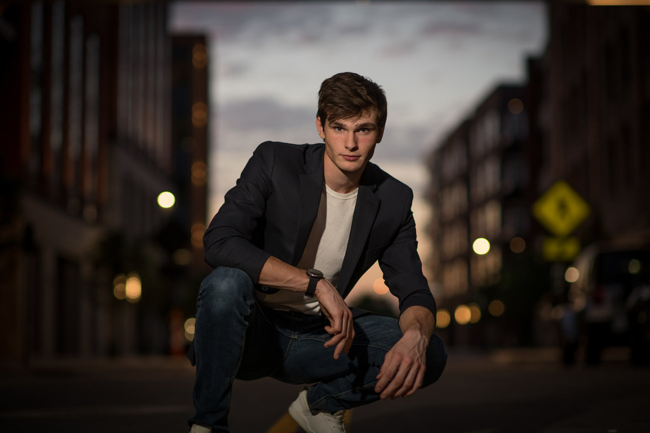 Teenage boy squatting at dusk on an urban street posing for senior pictures in Dublin OH.