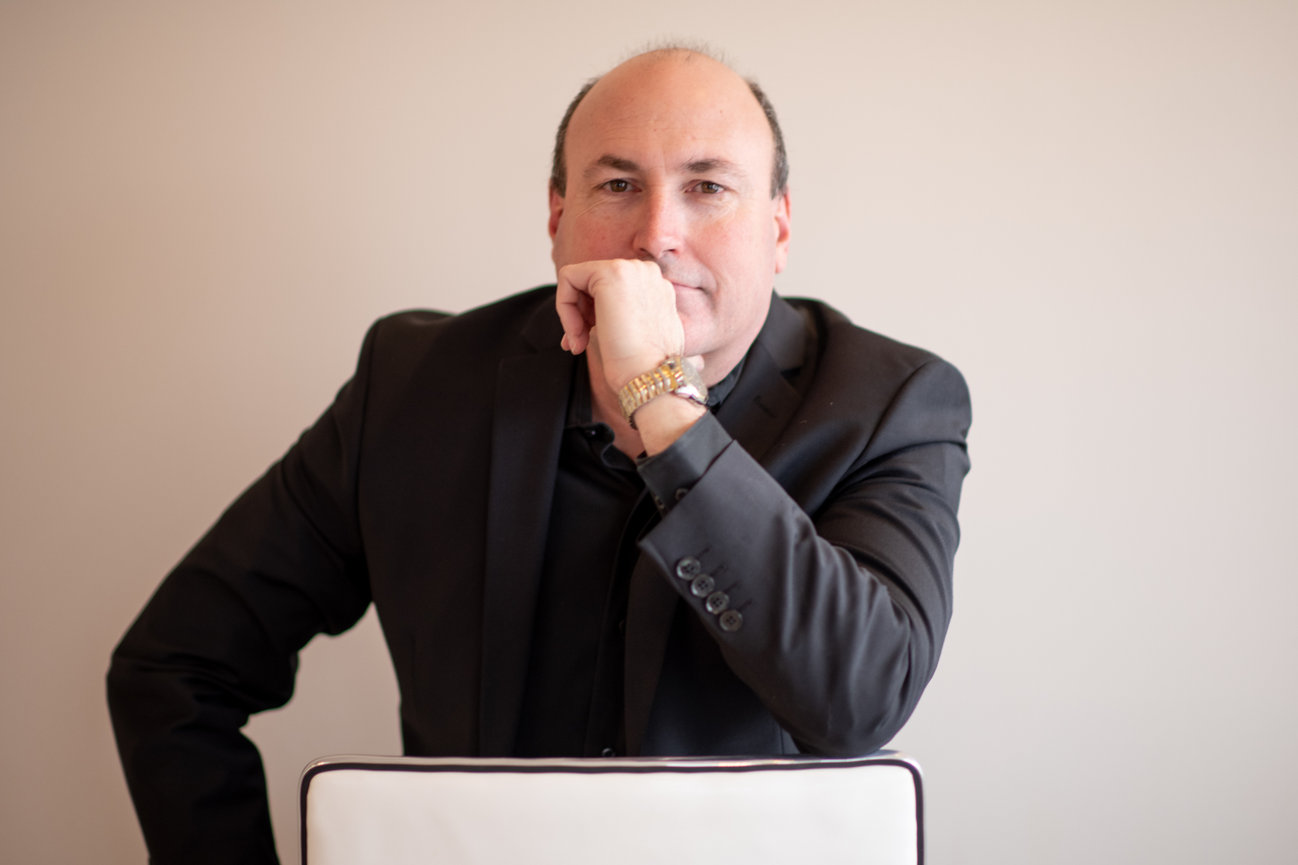 A man in a black suit resting his chin on his hand, posed thoughtfully against a light background for professional headshots in columbus and dublin ohio.