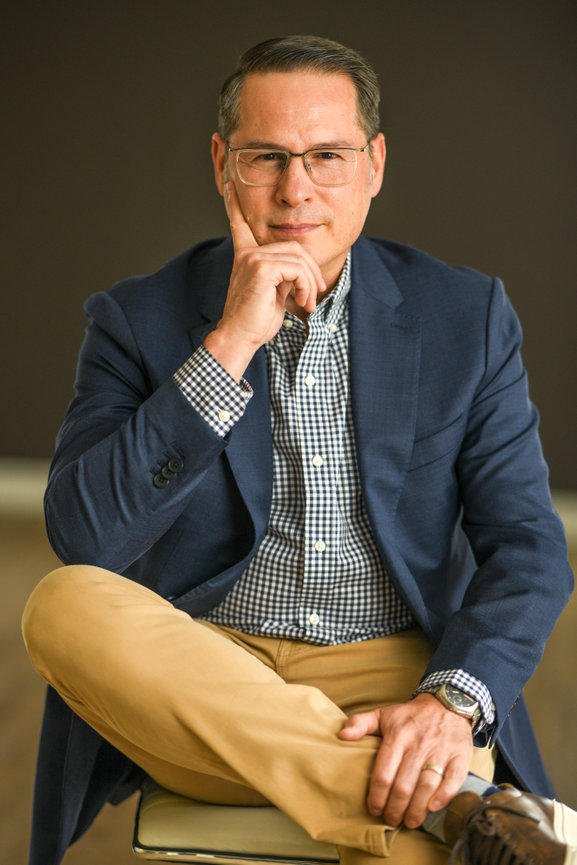 Man in a blazer and checked shirt sitting with one leg crossed, posing thoughtfully for professional headshots in dublin ohio