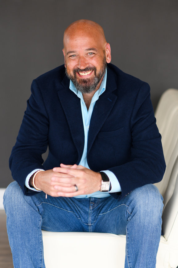 Smiling business professional in blazer and light blue shirt seated on sofa for professional headshots in Columbus Ohio