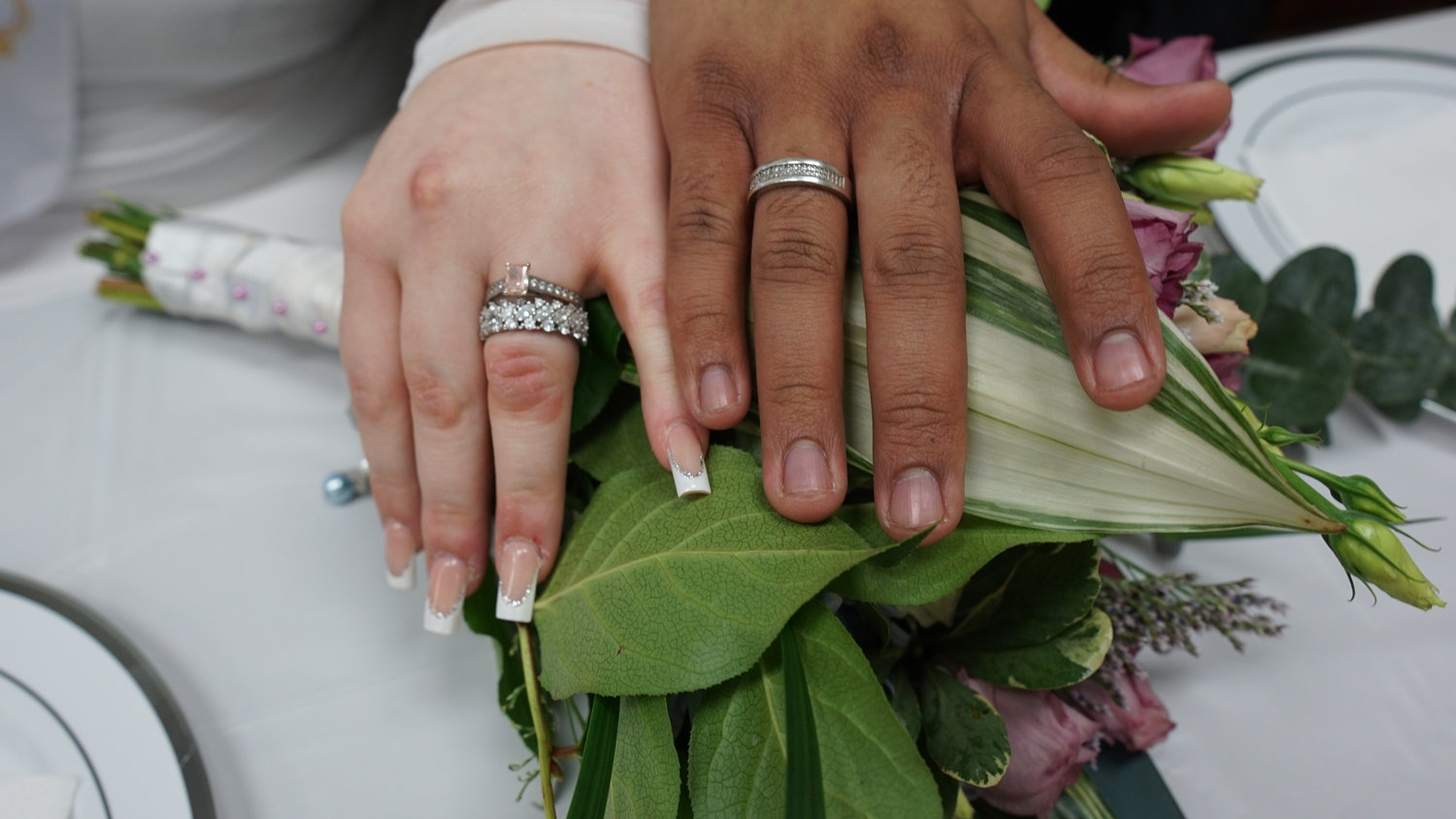 Close-up of bride and groom's hands with wedding rings holding a bouquet