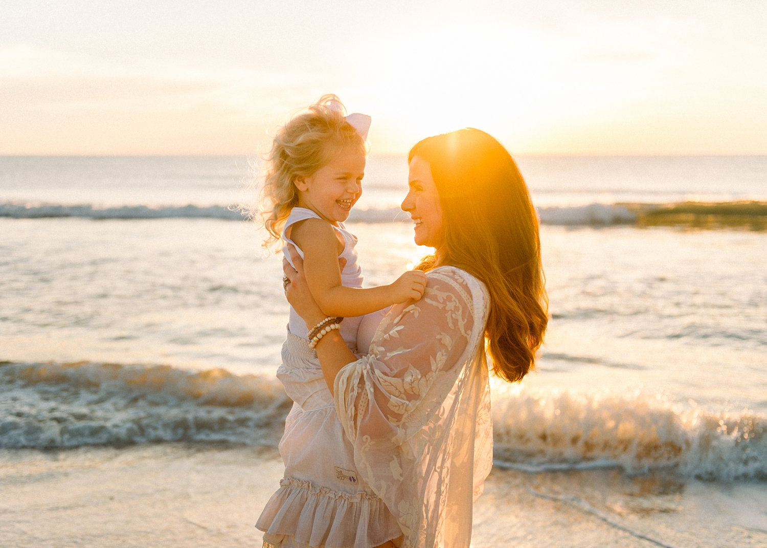 mom holding her daughter and smiling, the sun is rising over the Atlantic ocean