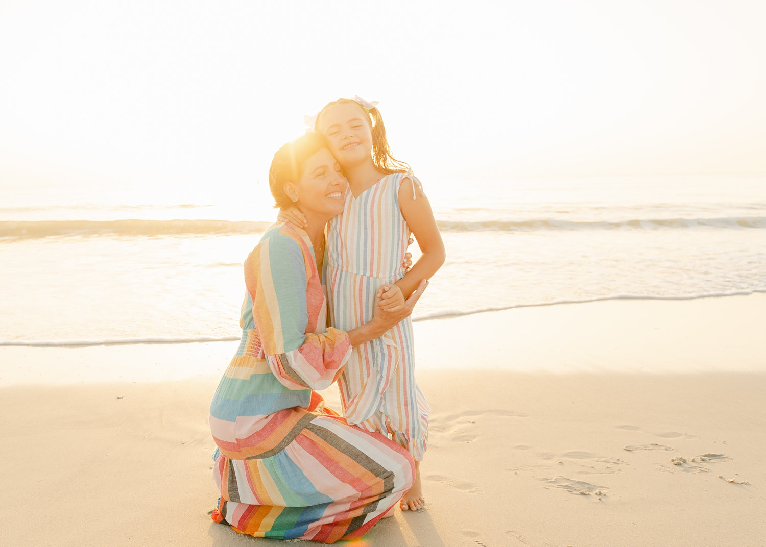 cancer survivor kneeling and hugging her daughter with the sun setting behind them